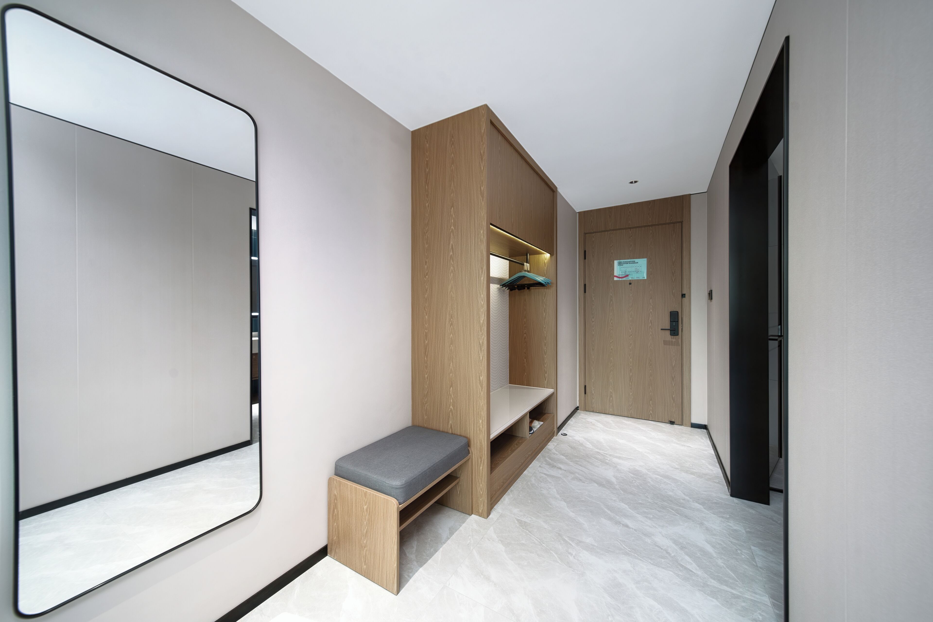 A modern hotel room with a large mirror, a wooden bench, and a built-in shelf.
