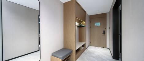 A modern hotel room with a large mirror, a wooden bench, and a built-in shelf.