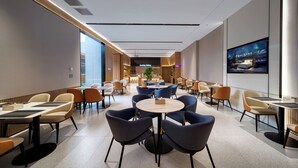 A modern hotel lobby with round tables, comfortable chairs, a large TV screen, and a kitchen area in the background. - Echarm International Hotel Guangzhou Huangpu Flagship Branch (Guangzhou)