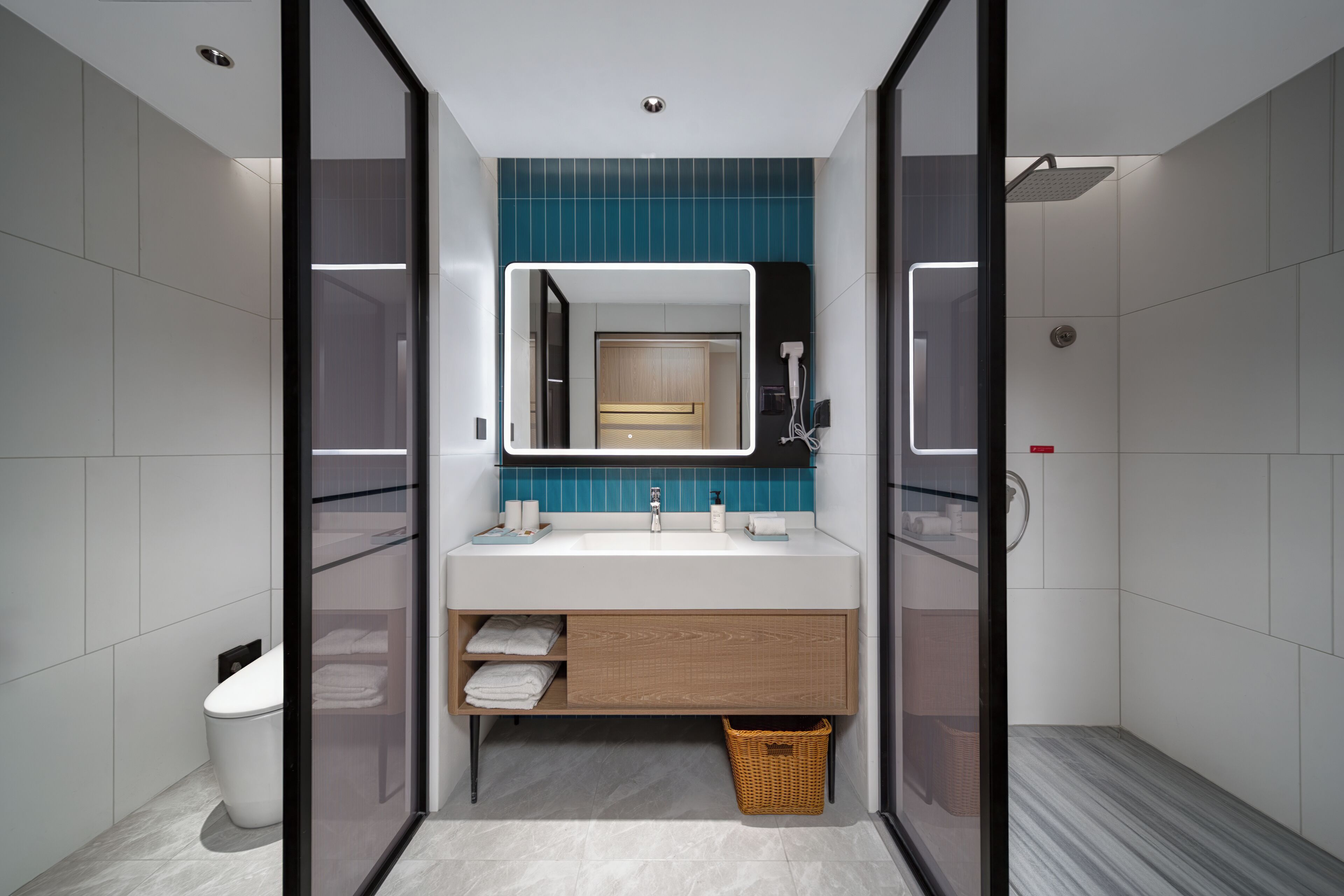 A modern bathroom with a glass-enclosed shower, a white sink with a mirror above it, and a wooden vanity with a basket.