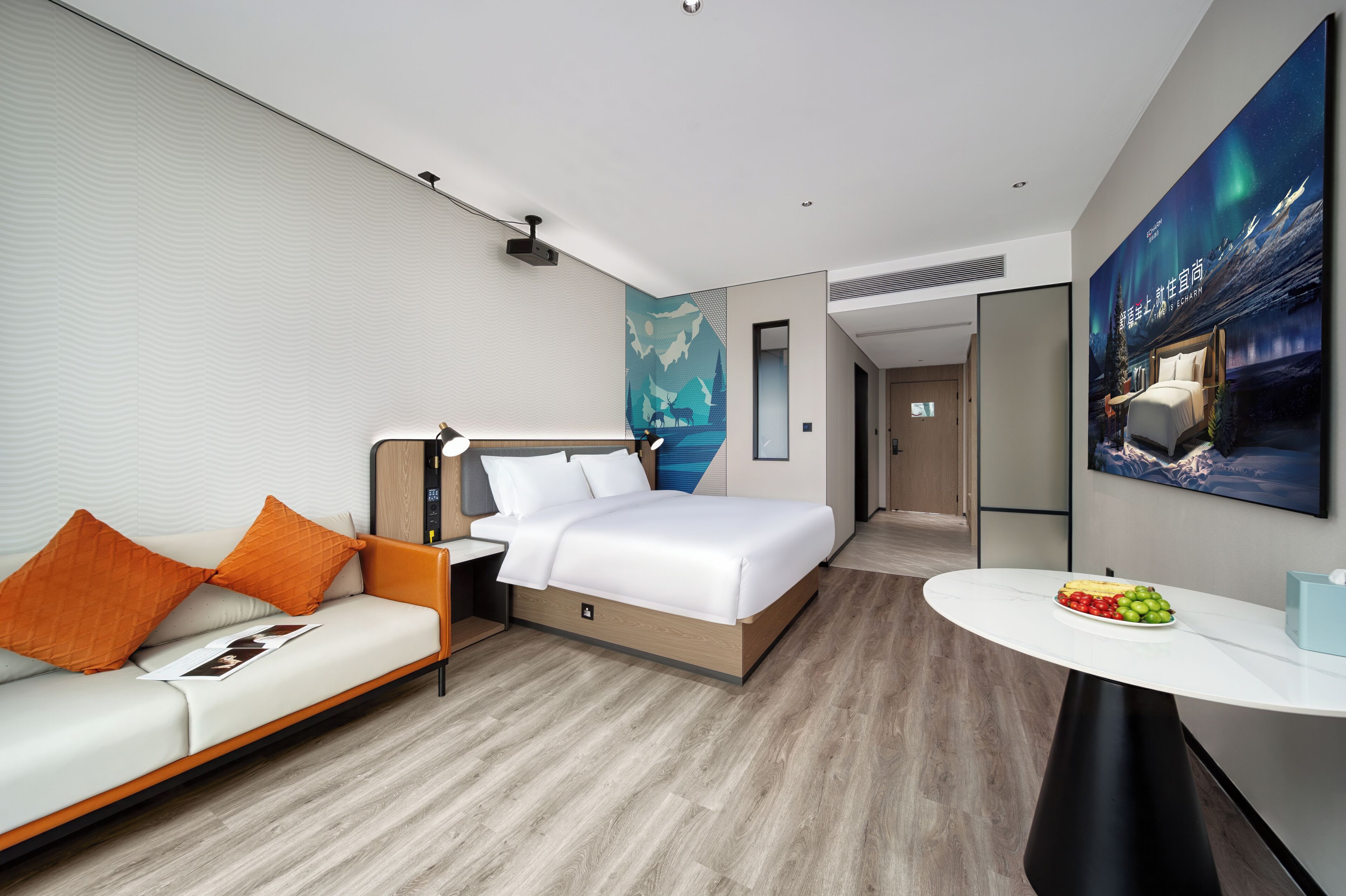 A modern hotel room with a bed, a sofa, a dining table, and a large painting on the wall.