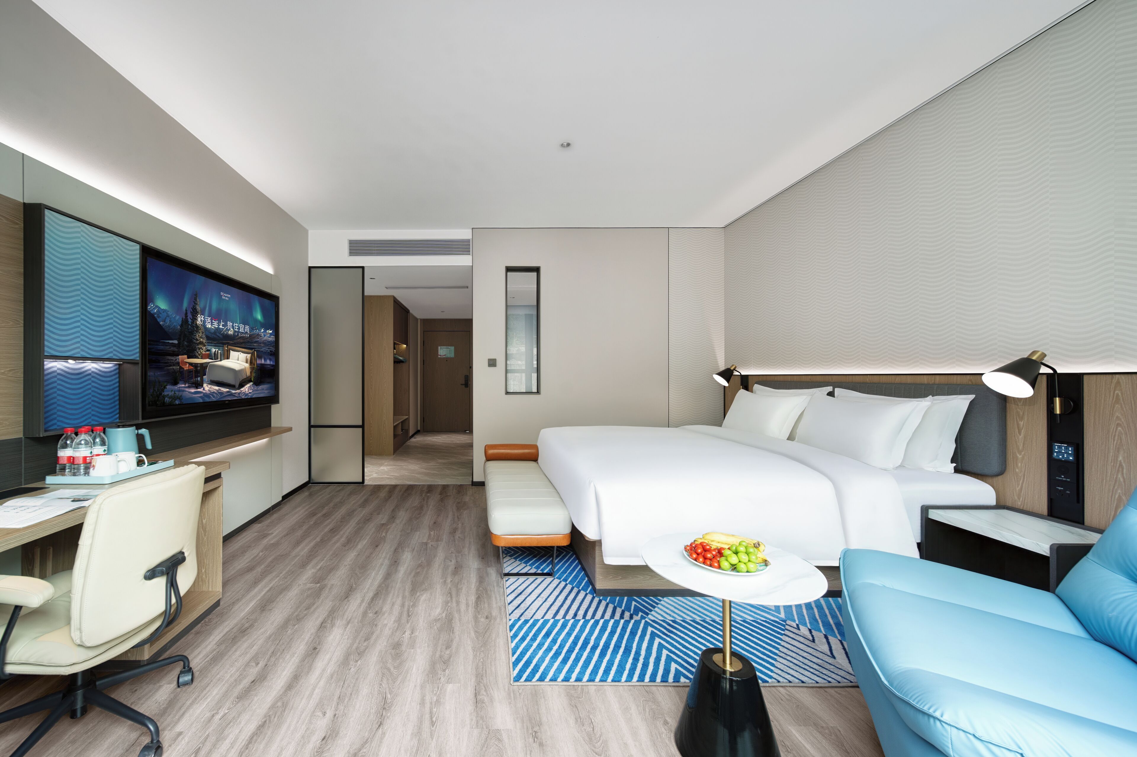 Une chambre d’hôtel moderne équipée d’un lit, d’un bureau avec un ordinateur, d’une télévision et d’un coin salon avec une table.