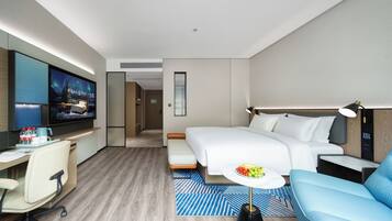 A modern hotel room with a bed, a desk with a computer, a TV, and a seating area with a table.