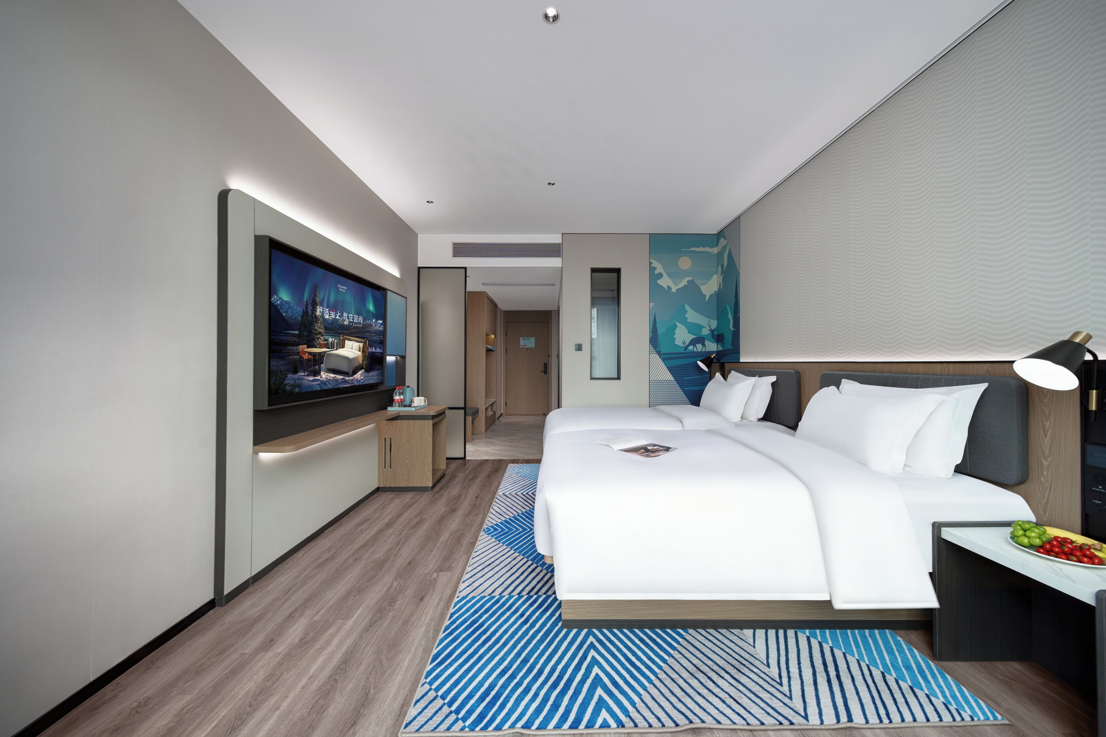 Une chambre d’hôtel moderne dotée d’un grand lit, d’un téléviseur à écran plat, d’un bureau avec une lampe et d’une œuvre d’art accrochée au mur.