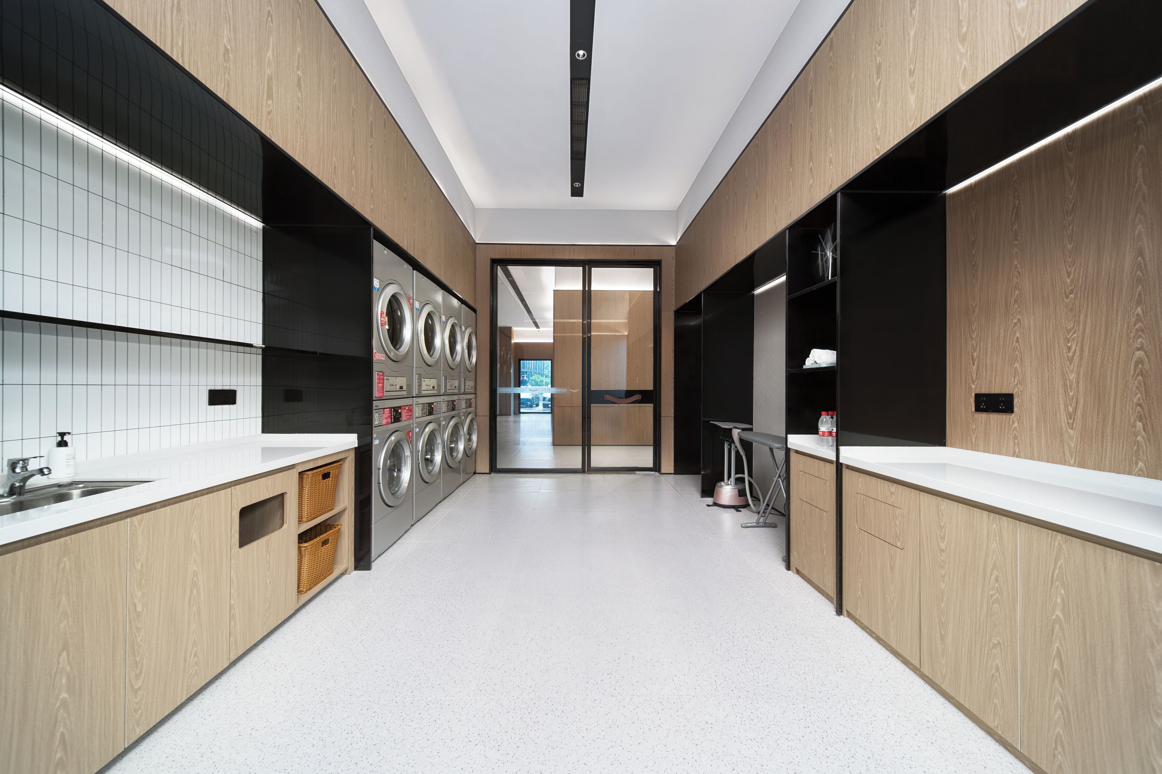 A modern laundry room with built-in washers and dryers, a sink, and a coffee machine.