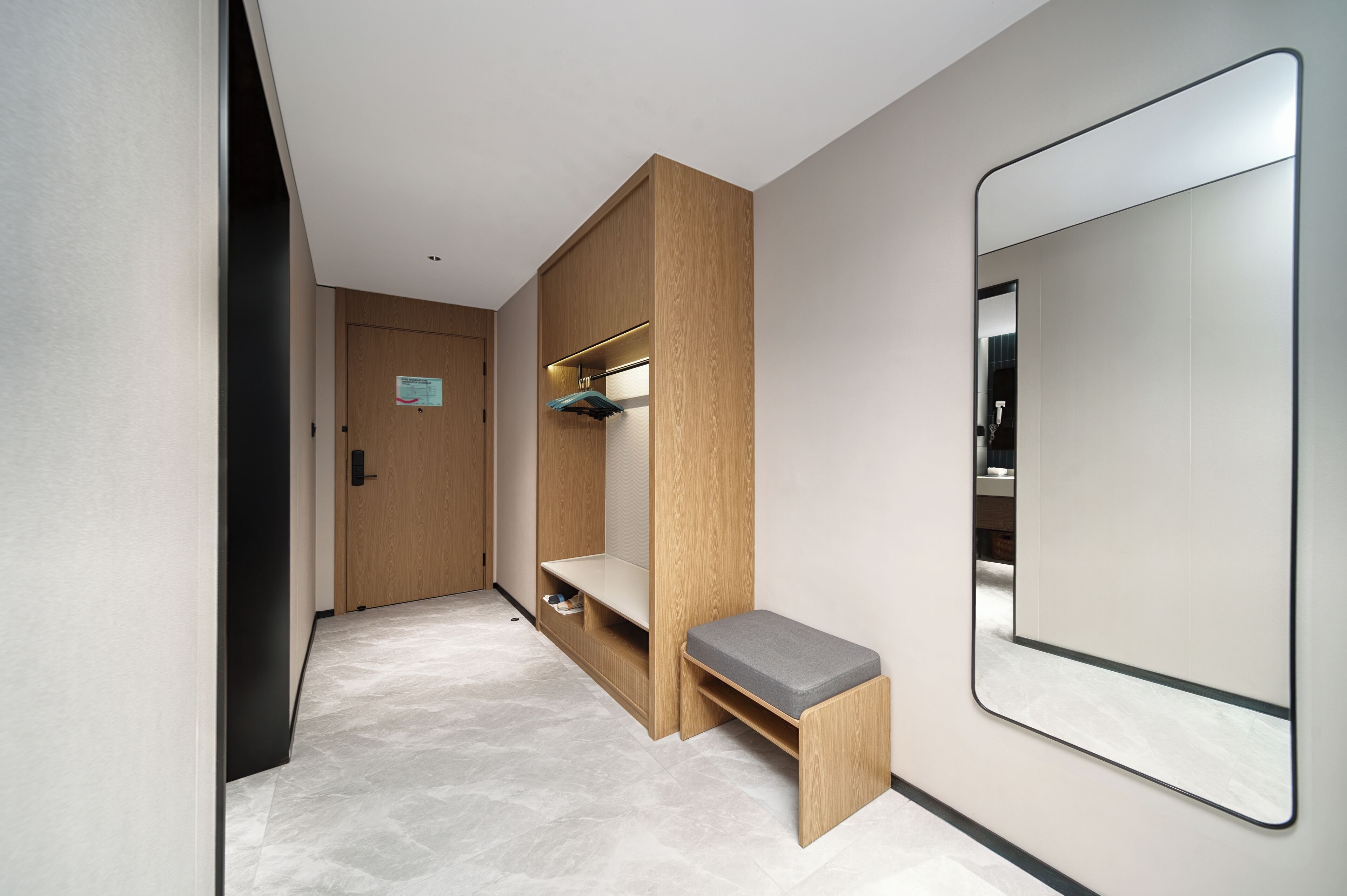 Un couloir avec un banc en bois, un miroir et une porte sur laquelle est apposée une pancarte.