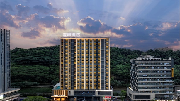 A modern hotel with a prominent vertical design, surrounded by lush greenery and other buildings. - Echarm International Hotel Guangzhou Huangpu Flagship Branch (Guangzhou)