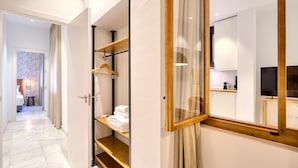 Habitación de hotel con piso de mármol, un estante de madera con toallas, un espejo y vista al baño.