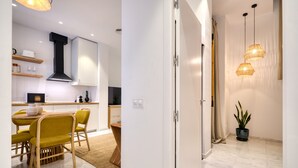 Cocina moderna con armarios blancos, extractor de aire negro y comedor con sillas amarillas y mesa de madera.