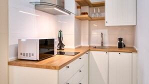 A modern kitchen with white cabinets, a wooden countertop, a microwave, a kettle, and a glass shelf with kitchenware.