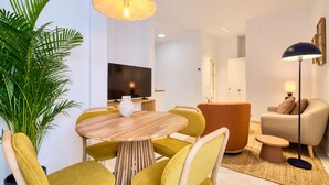 A modern living room with a round wooden table, yellow chairs, a large potted plant, a television, and a sofa with a lamp.