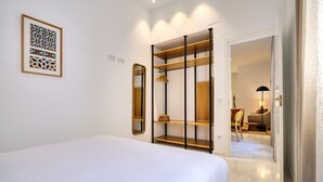 A bedroom with a bed, a wardrobe with shelves, a mirror, and a framed artwork on the wall.