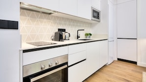 Uma cozinha moderna com armários brancos, bancada preta, forno embutido, micro-ondas e cafeteira.
