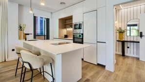 Una cocina moderna con armarios blancos, una isla central con taburetes altos, electrodomésticos integrados y una pared de acento de madera.