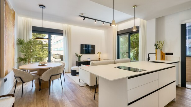 Una cocina moderna con una isla central, comedor con sillas y un sofá.