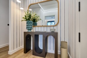 Un comptoir d’accueil moderne agrémenté d’un grand miroir, d’un vase contenant des feuilles vertes et d’un luminaire.