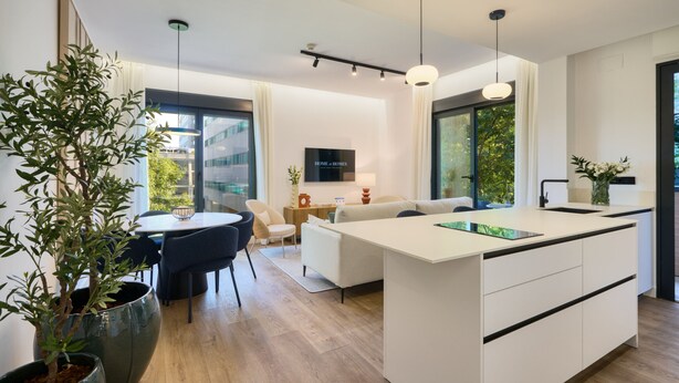 Una cocina moderna con una isla central, comedor con sillas, un sofá y un ventanal grande.