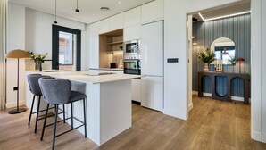 A modern kitchen with white cabinetry, a central island with bar stools, built-in appliances, and a wooden floor. - Viapol Homes 3.1 by Home at Homes (Sevilla)