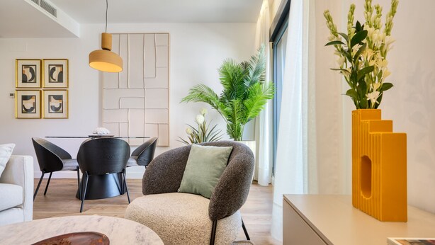 A modern living room with a sofa, a coffee table, a dining area with chairs, a plant, and a vase with flowers. - Viapol Homes 3.1 by Home at Homes (Sevilla)