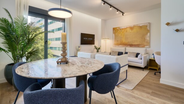 Un soggiorno moderno con un tavolo rotondo in marmo, poltrone blu, un divano bianco e un grande quadro astratto appeso al muro.