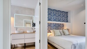 Una camera da letto moderna con un letto grande, un comodino e un tavolino. C'è un bagno con un lavandino e uno specchio.