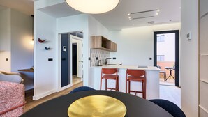 A modern interior with a dining area featuring a black table and a gold bowl, a kitchen with wooden cabinets, and a view of the outdoors. - Viapol Homes 3.2 by Home at Homes (Sevilla)
