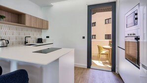 Et moderne køkken med en hvid bordplade, armatur i sort og et indbygget ovn. Der er en skydedør til en altan med en gul stol og et bord.