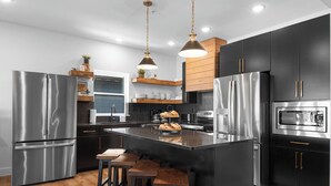 A modern kitchen with stainless steel appliances, a central island with stools, and pendant lighting.