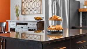 A kitchen with a stainless steel refrigerator, a wooden serving tray with donuts, and a potted plant.