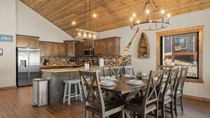 A modern kitchen with wooden cabinets, a stainless steel refrigerator, and a dining area with a wooden table and chairs. - 2BR Retreat Near SDC w/ Hot Tub + Boat Slip (Branson)