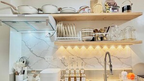 A modern kitchen with a white countertop, a built-in stove, a sink, and a wooden shelf above the countertop.