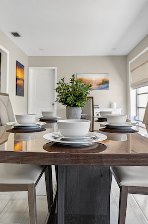A dining table with white bowls and plates, a potted plant, and a painting on the wall.