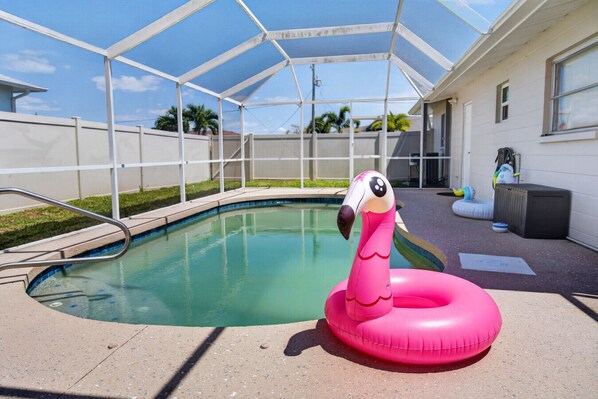A swimming pool with a pink flamingo float, surrounded by a covered area with a white fence.