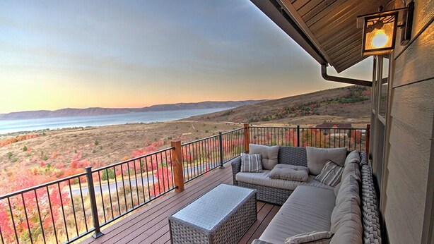 A balcony with wicker furniture, a view of a lake, and a sunset.