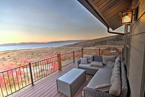 A balcony with wicker furniture, a view of a lake, and a sunset.