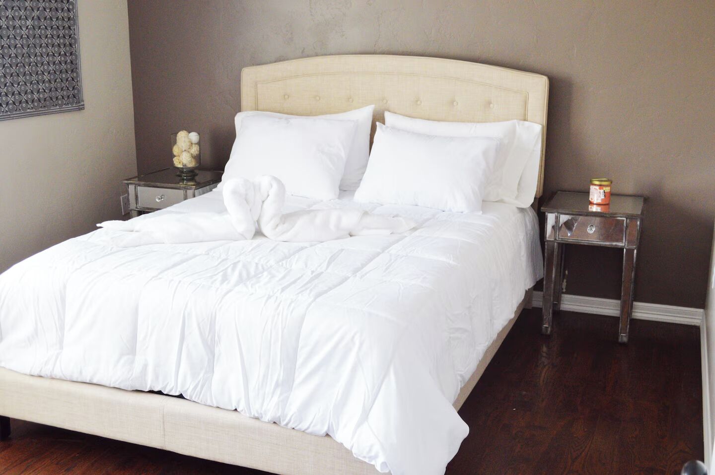 A neatly made bed with white bedding, a headboard, and two bedside tables with a small decorative item on one.