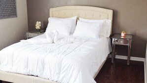 Un letto rifatto con biancheria bianca, una testiera e due comodini, uno dei quali con un piccolo oggetto decorativo.