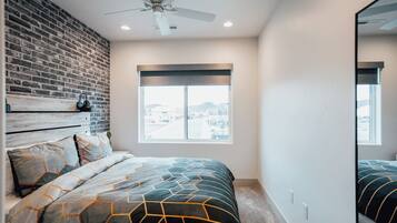 A bedroom with a brick wall, a large window, a ceiling fan, and a bed with patterned bedding.