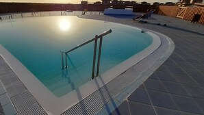 Una piscina con una escalera de metal y un flotador salvavidas, rodeada por un solárium de baldosas.