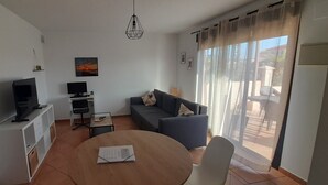 Una sala de estar moderna con sofá, televisor, una mesita y una mesa de comedor.