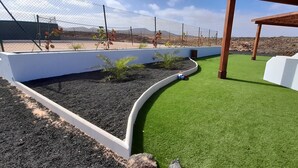 Un jardín ajardinado con césped artificial, una pared blanca y una estructura de pérgola.