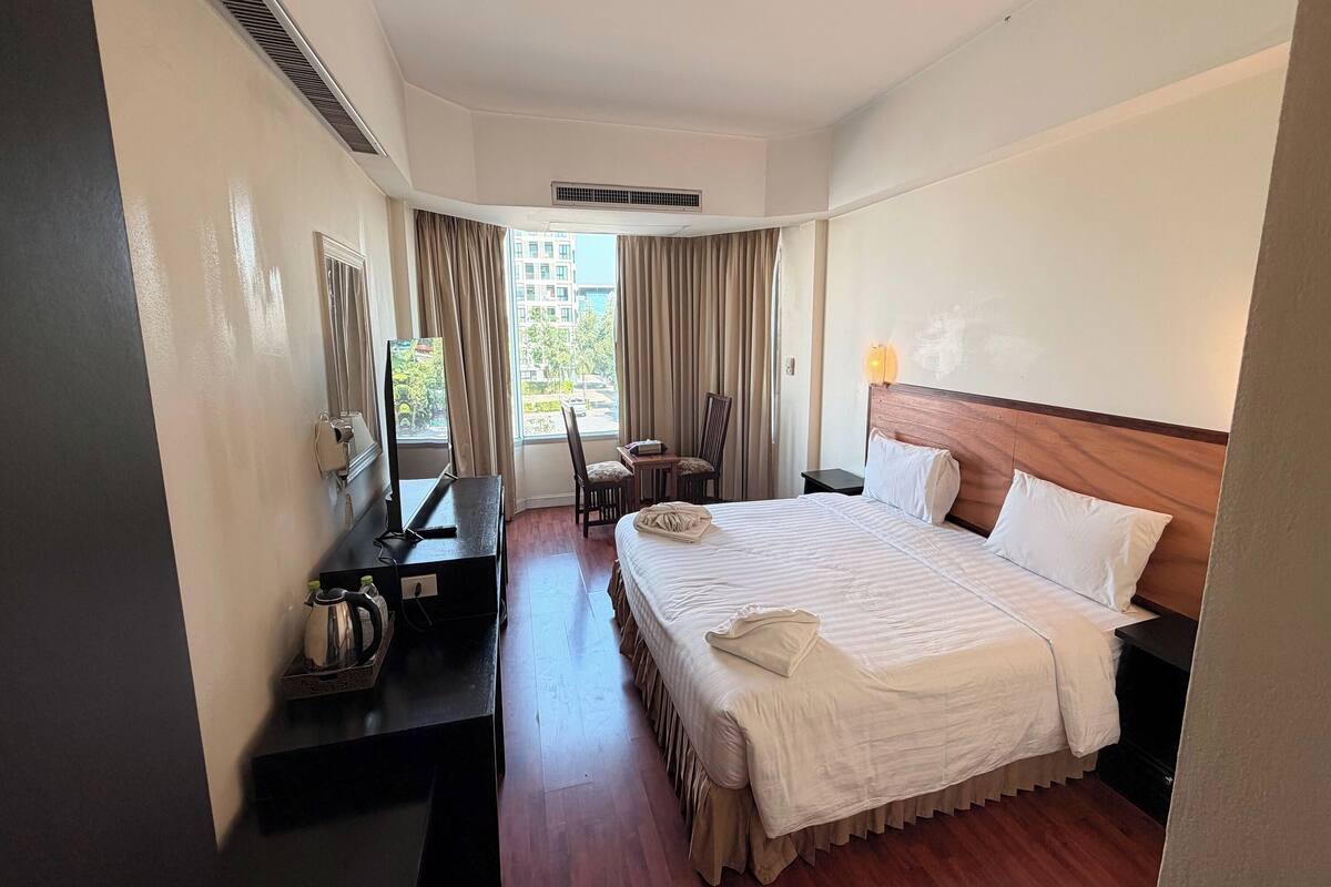 A hotel room with a bed, a desk, a chair, a small table, and a window with curtains.
