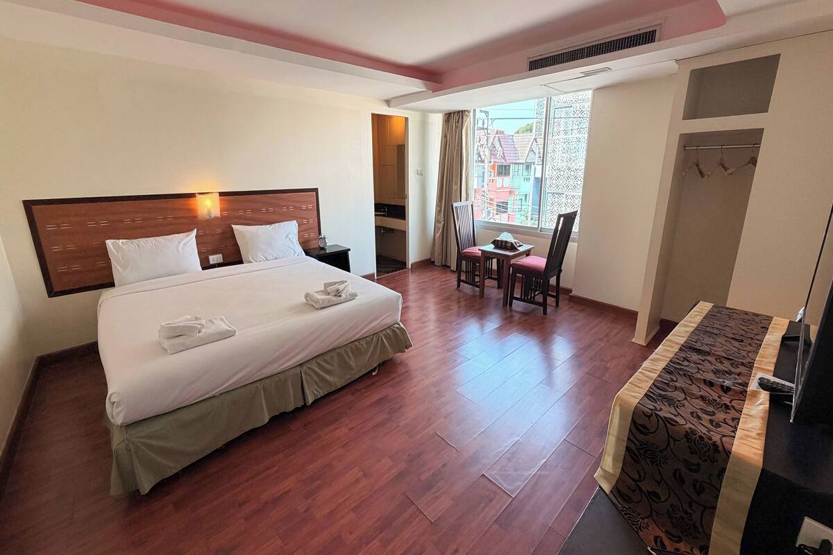 A hotel room with a bed, a desk, a chair, a window with a view, and a wardrobe.