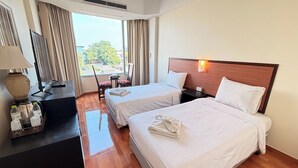 Habitació d'hotel amb dos llits, un escriptori amb una làmpada, una cadira i una finestra amb cortines.