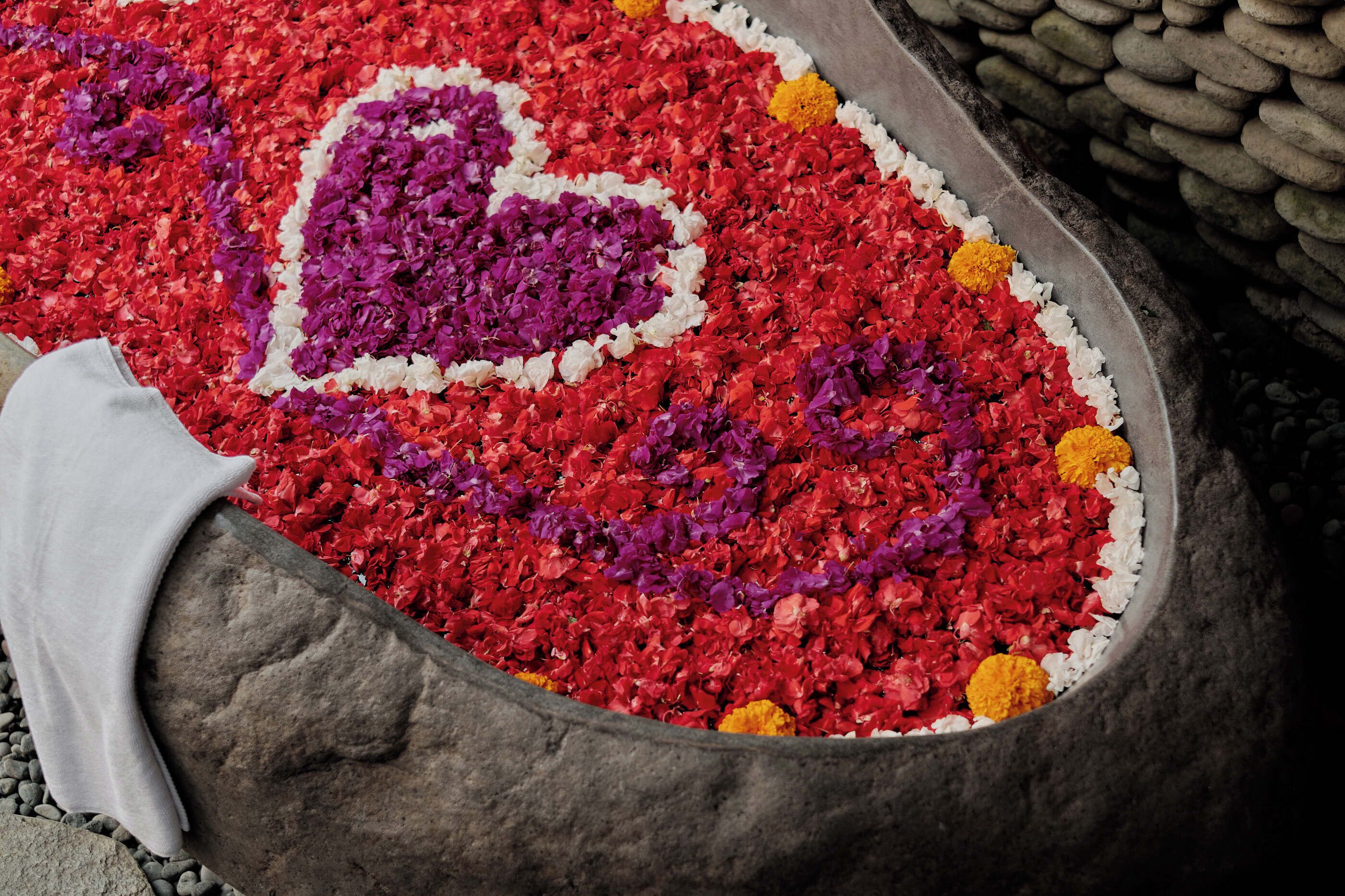 A stone basin filled with red, purple, and yellow flower petals arranged in a heart shape.
