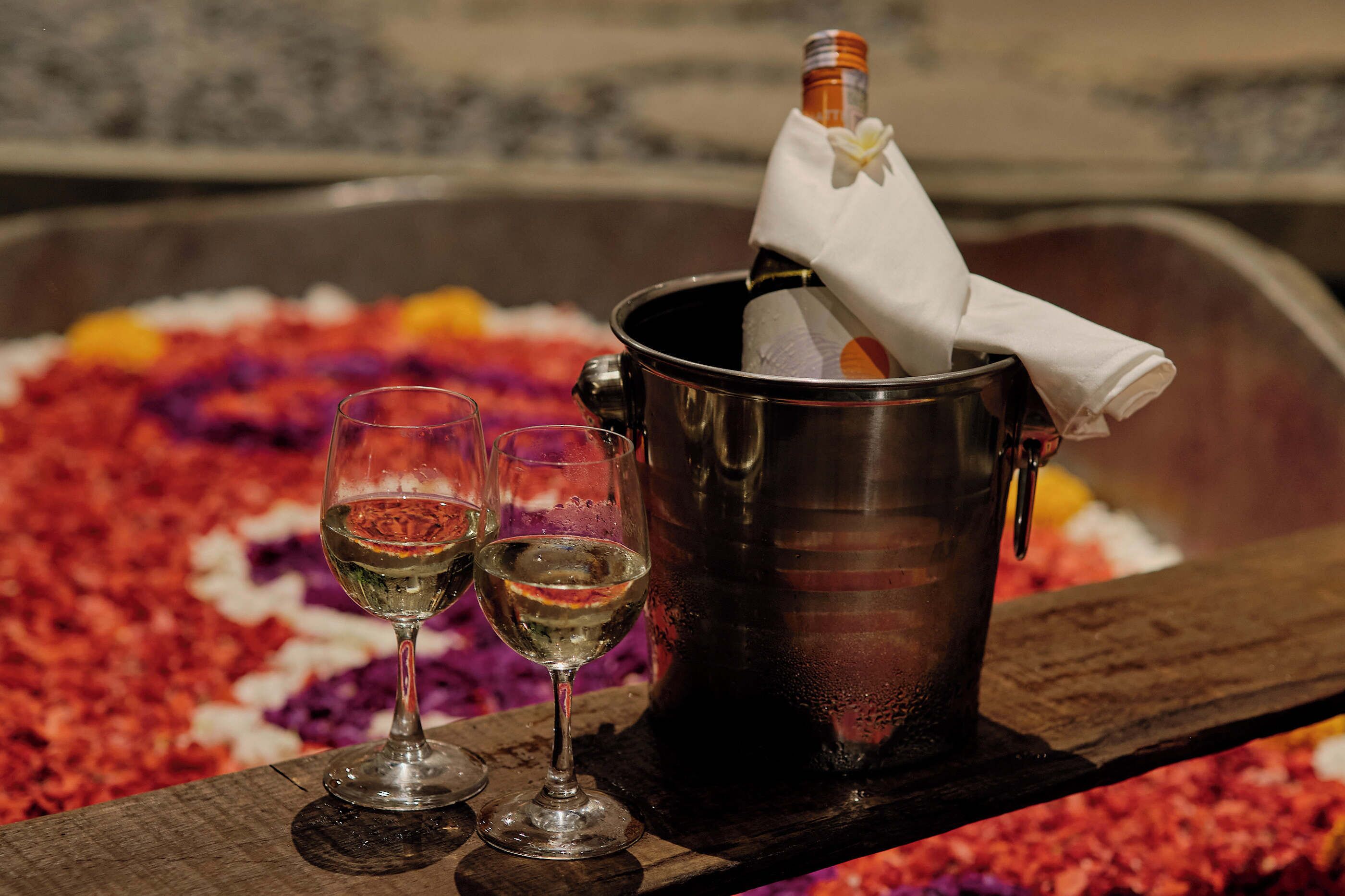 A metal bucket with a bottle of champagne and two glasses of wine on a wooden surface.