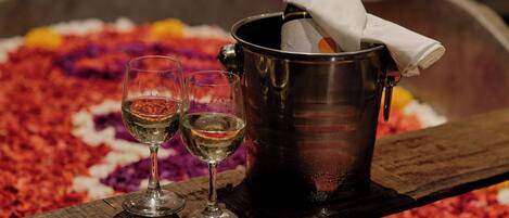 A metal bucket with a bottle of champagne and two glasses of wine on a wooden surface.