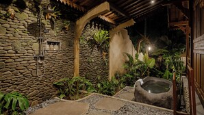 A stone-walled spa area with a hot tub, surrounded by tropical plants and a wooden archway. - Hidden Saren Villa Ubud (Ubud)