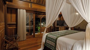 A bedroom with a bed, curtains, a TV, and a wooden floor. - Hidden Saren Villa Ubud (Ubud)