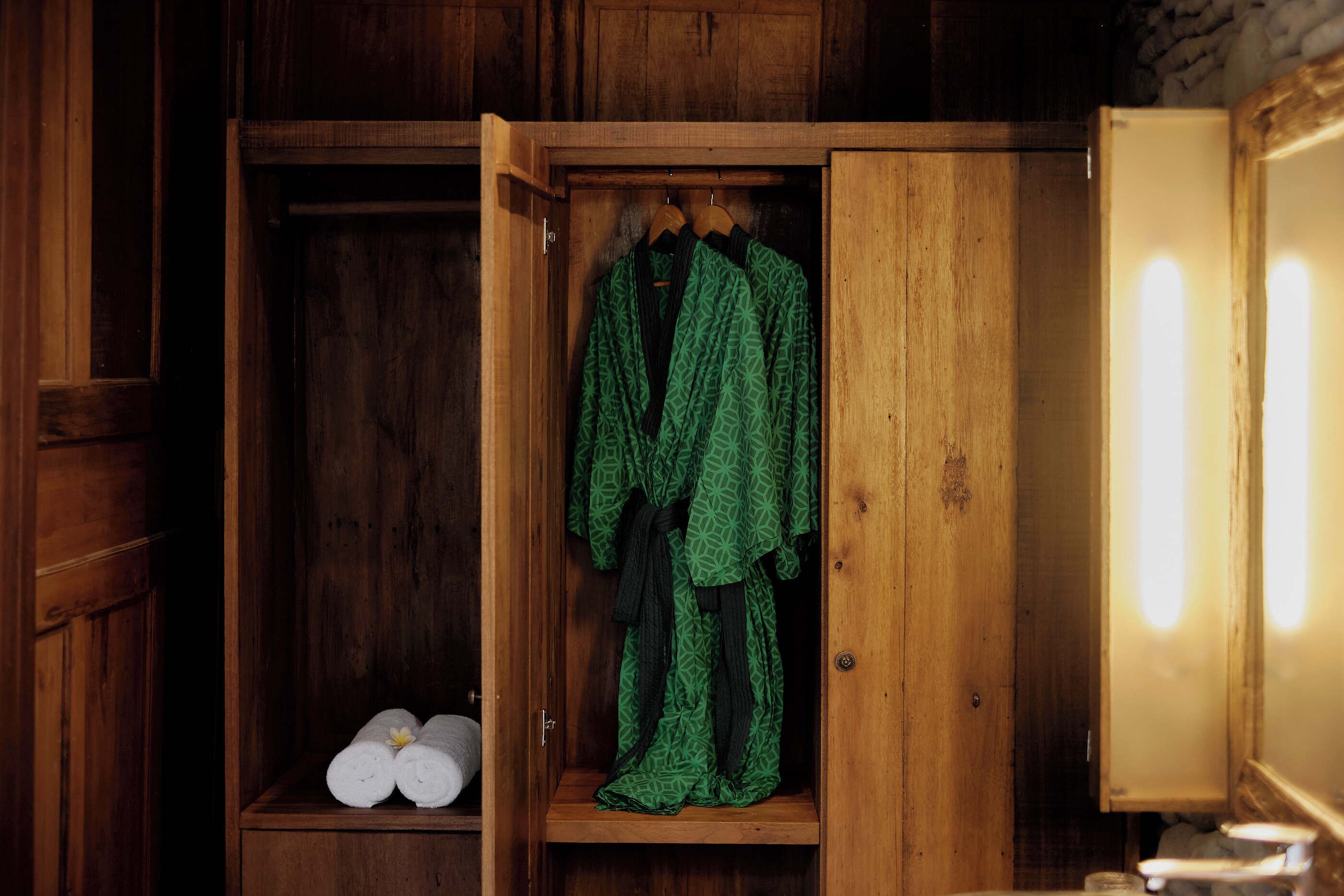 Une armoire en bois avec un miroir et une étagère où sont rangées des serviettes enroulées.